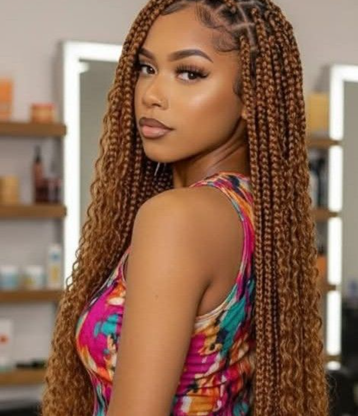 Woman with long, brown box braids; colorful top, looking over her shoulder.