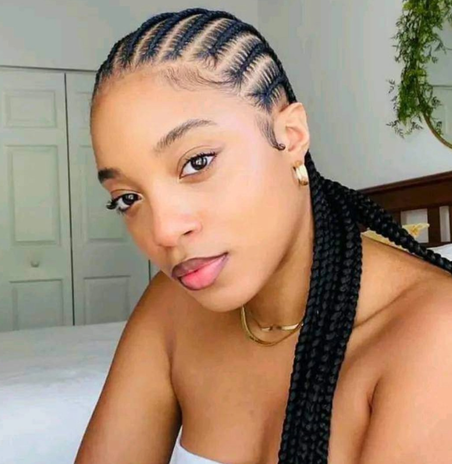 Woman with braided hairstyle looking at the camera, wearing gold jewelry, white top.