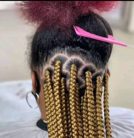 Close-up of a person's head, showing braided blonde extensions, and scalp with decorative parting.