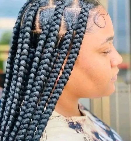 Woman with large, black box braids and a swirl design on her forehead.