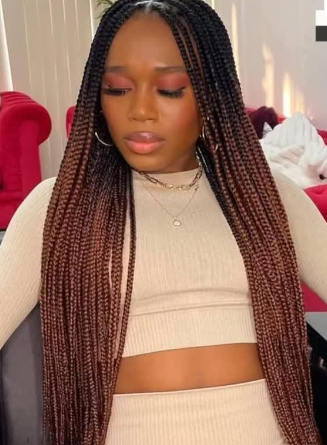 Woman with long box braids, transitioning from black to brown, wearing a cream-colored crop top and skirt.