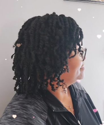 Woman with dark twisted hair, wearing glasses, and smiling slightly.