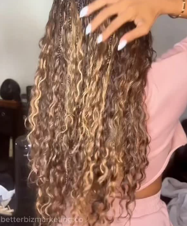 Woman with long, curly, highlighted hair, touching her head.