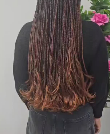 Person wearing a black sweater and denim skirt, with long braided hair that is brown and ombre, flowing at the ends.