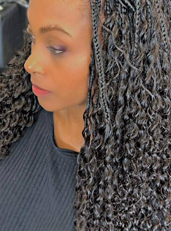 Woman with long, curly black hair, wearing a black shirt. She looks off to the side, with neutral expression.
