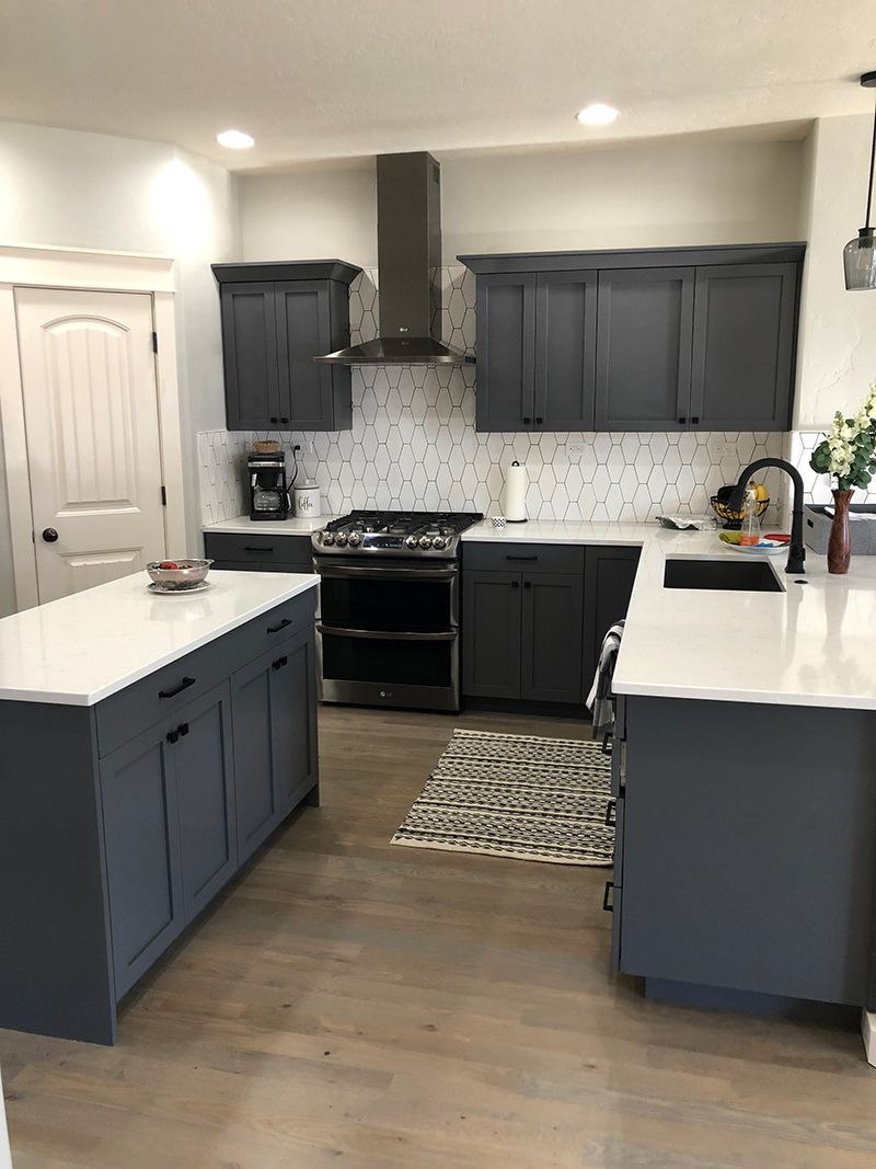 a kitchen with gray cabinets , white counter tops , a stove and a sink .