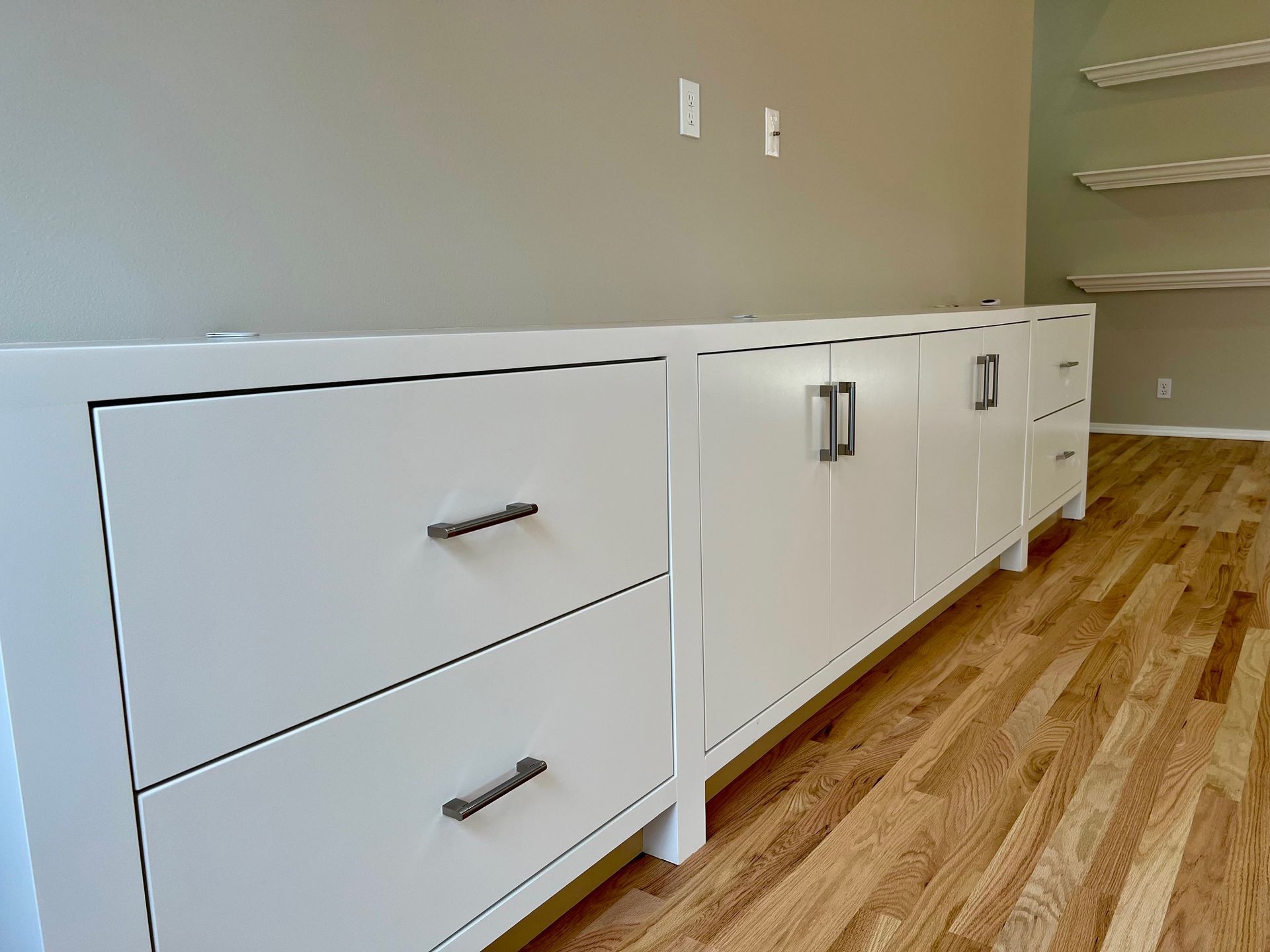 a long white dresser with drawers and cabinets in a room with hardwood floors .