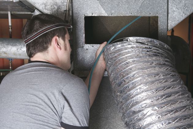 Worker installing ducting in an attic with insulated silver ventilation hose and exposed pipes