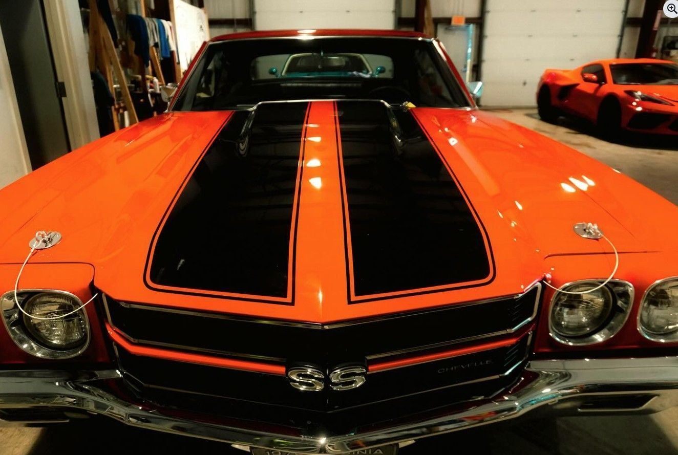 Orange classic muscle car with black racing stripes, chrome grill, and hood pins.