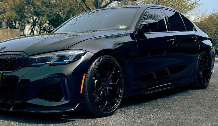 Black BMW sedan, lowered, with black rims, parked on asphalt.