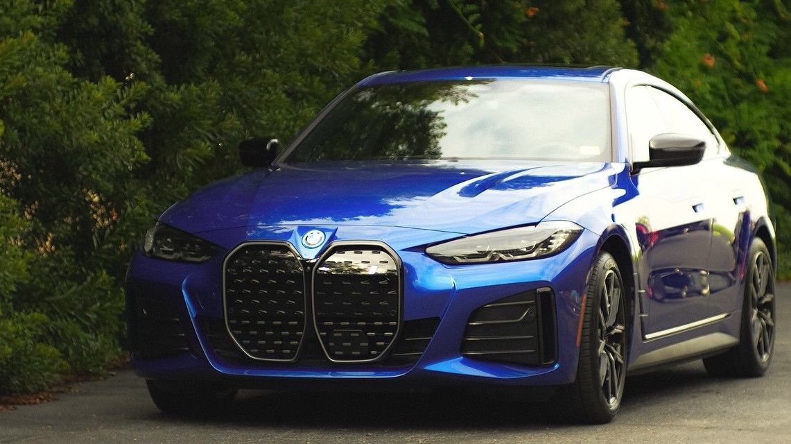 Blue BMW car parked on a road with green bushes in the background.