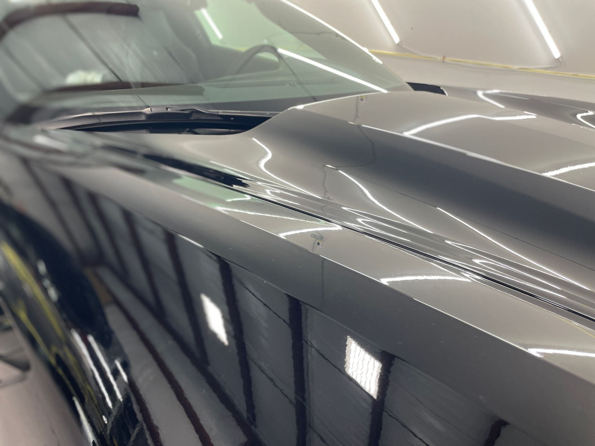 Black car hood reflecting overhead lights, highlighting its glossy finish.