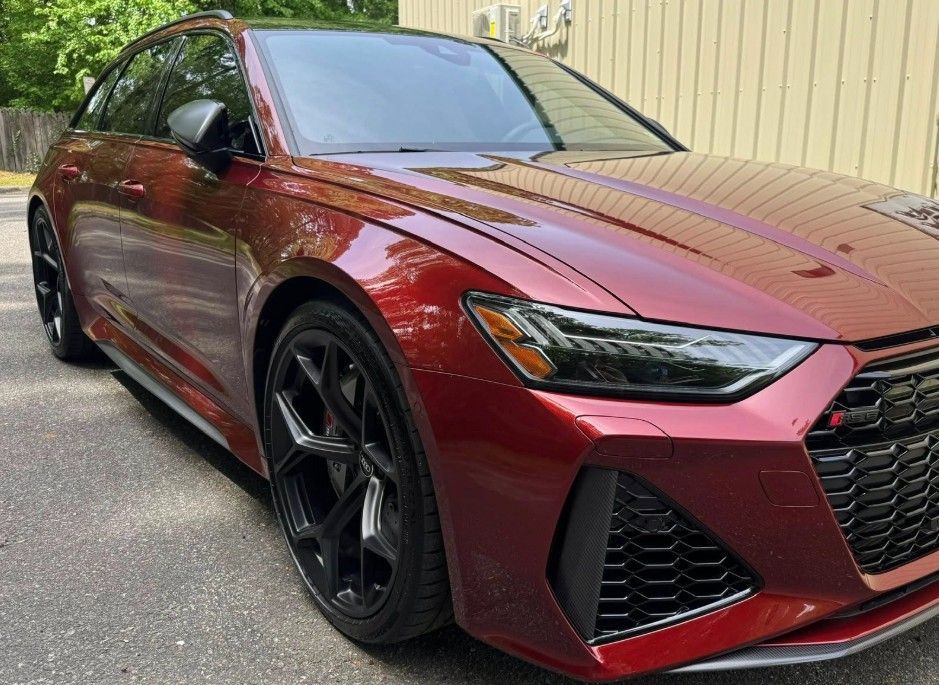 Red Audi RS 6 Avant station wagon, parked on asphalt, shiny paint, black wheels, in front of a building.