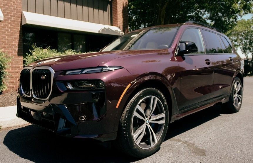 Burgundy BMW X7 SUV parked in front of a brick building.