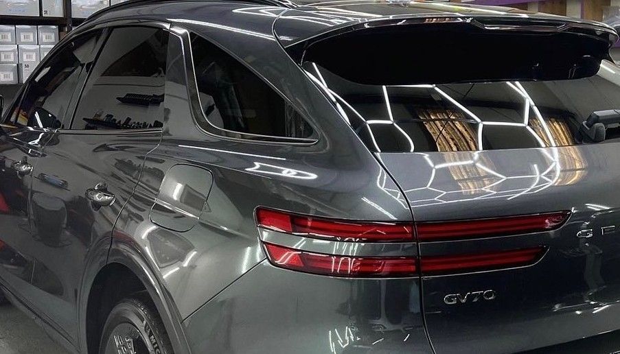 Grey Genesis GV70 SUV, rear view, taillights illuminated, shiny finish.