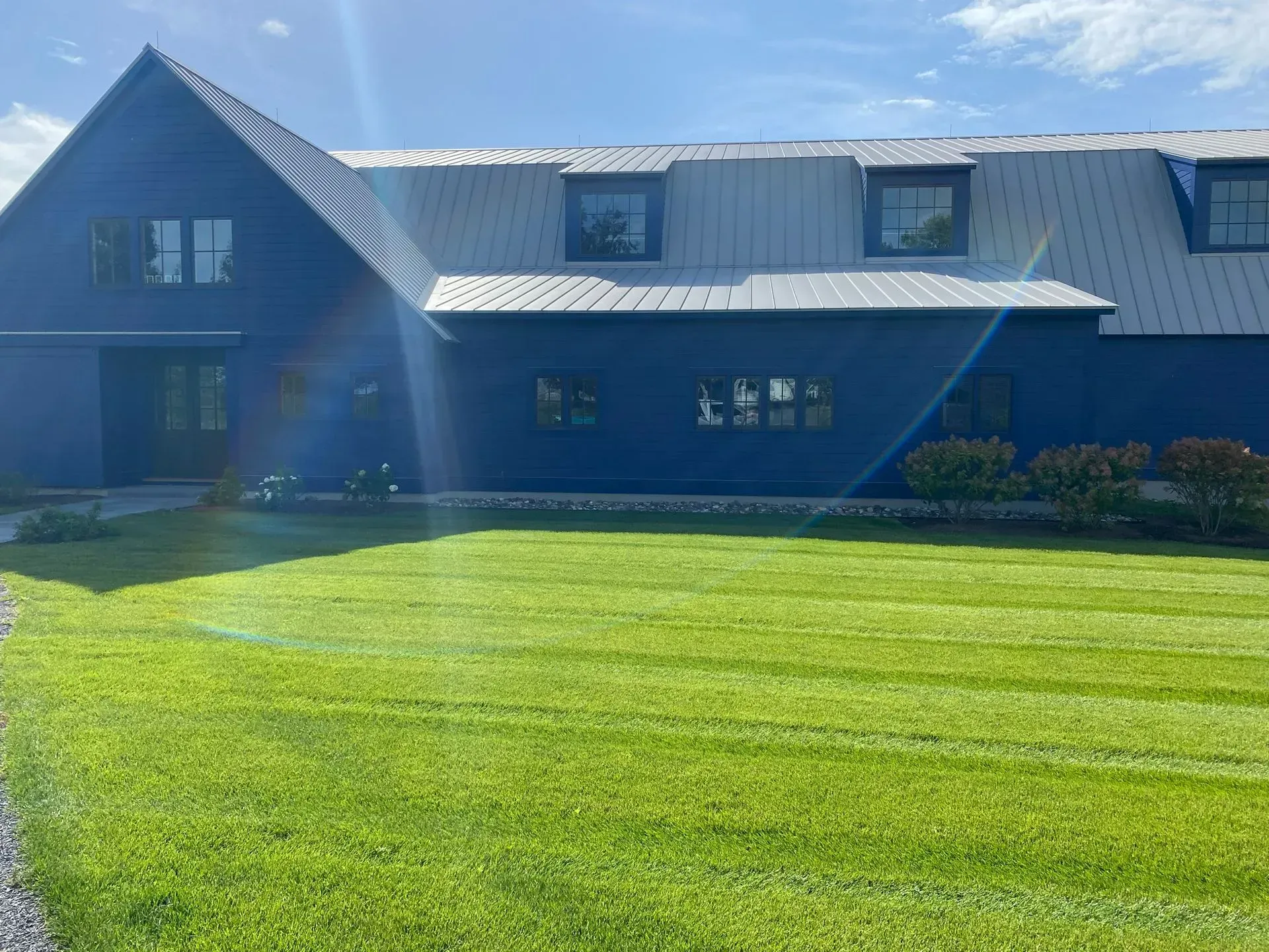 A two-story blue building with a metal roof and dormer windows, set behind a bright green lawn.
