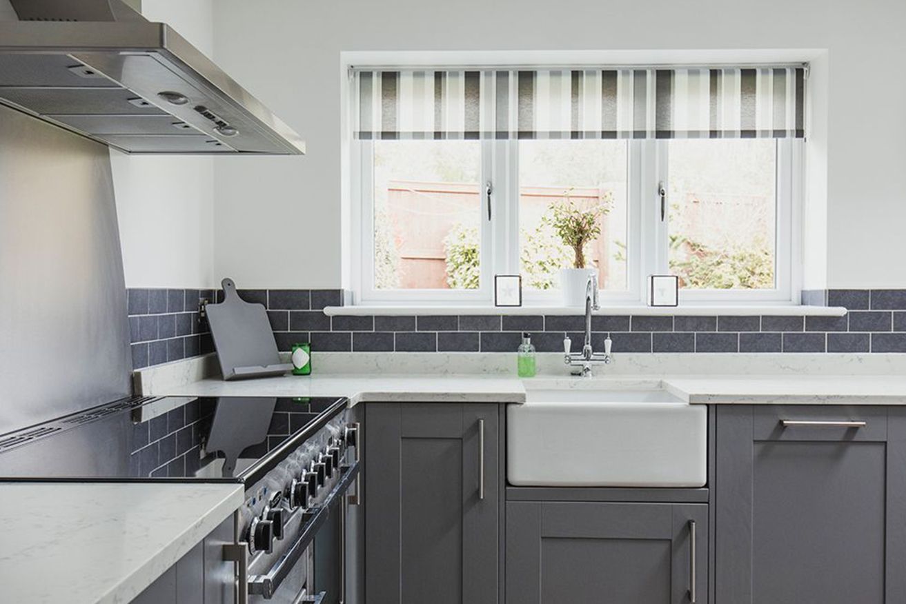 A kitchen with gray cabinets , a stove , a sink and a window.