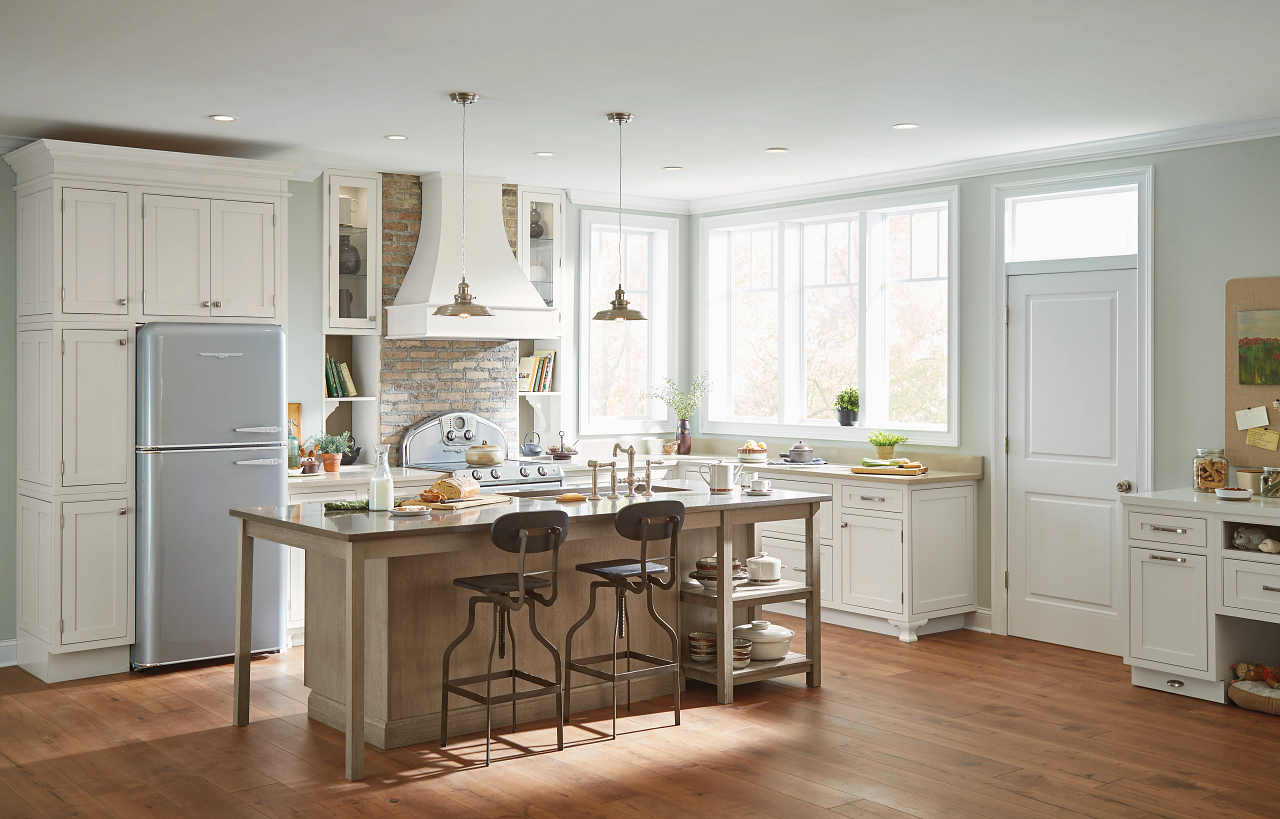 A kitchen with white cabinets , stools , a refrigerator , and a large island.