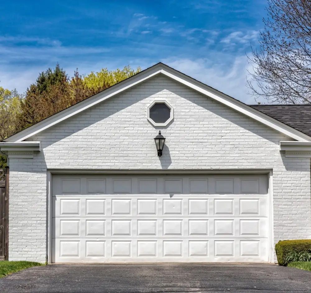 White garage with a closed door and a black light fixture, under a blue sky.