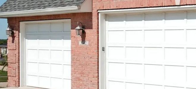 Garage with two white doors, red brick exterior, and gray roof.