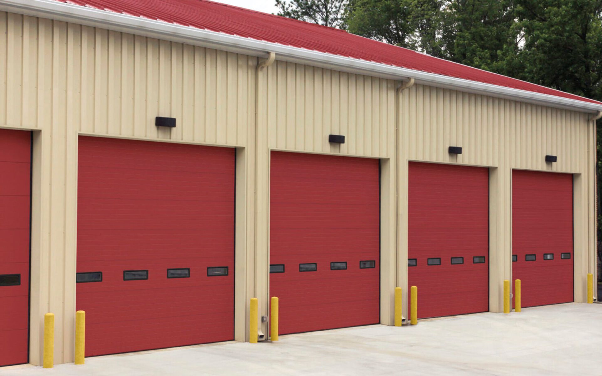 Fire station with beige walls, red doors and roof. Yellow poles flank each garage door.