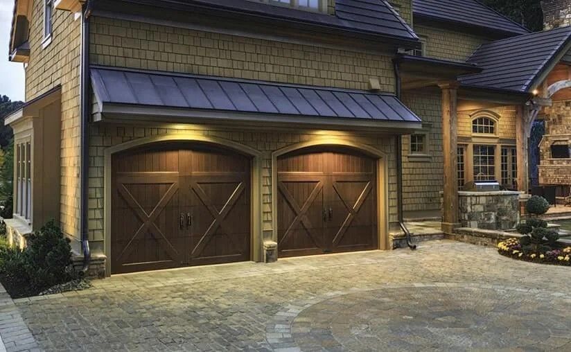 Two brown garage doors with lights, beige exterior, and a stone driveway.