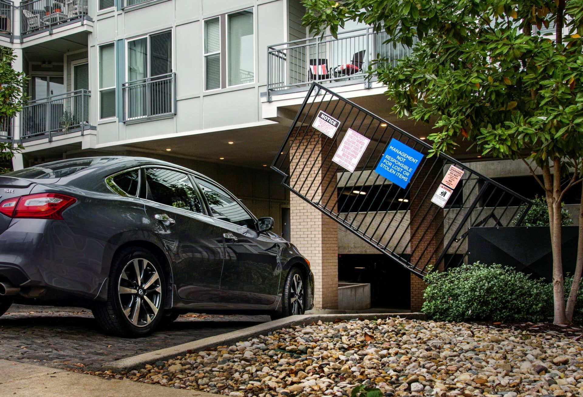 A car is parked in front of a building with a broken fence.