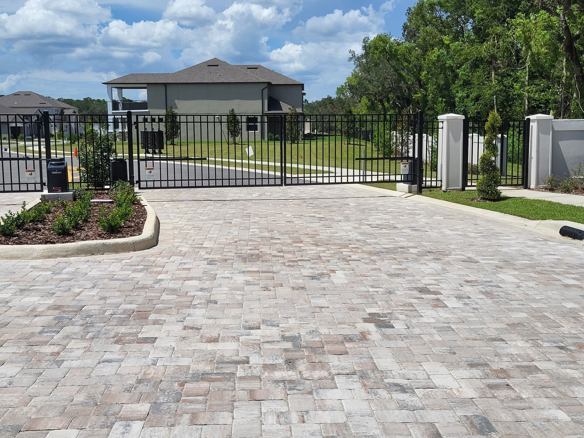 A brick driveway with a metal gate in front of a house