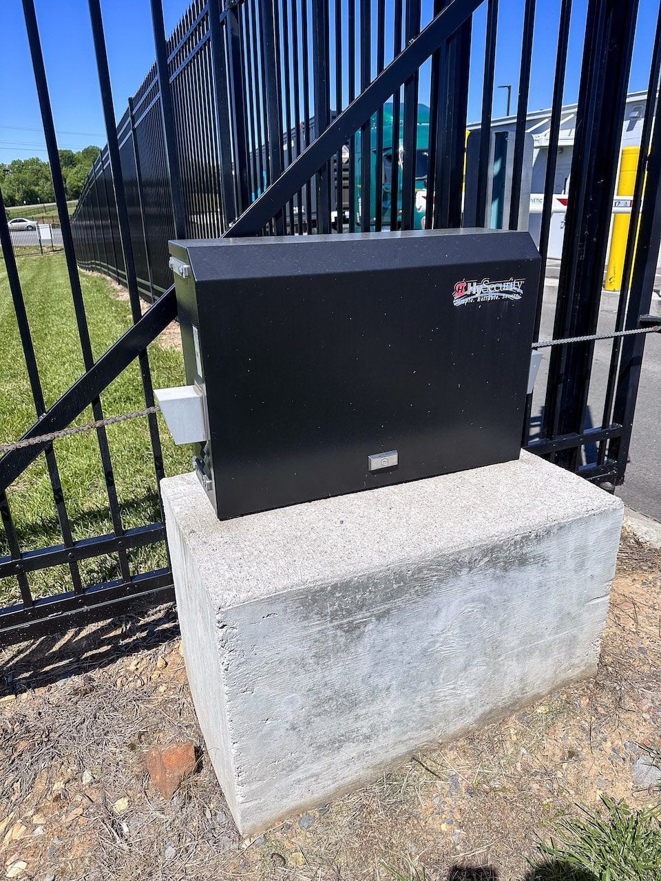 A black box is sitting on top of a concrete block next to a fence.