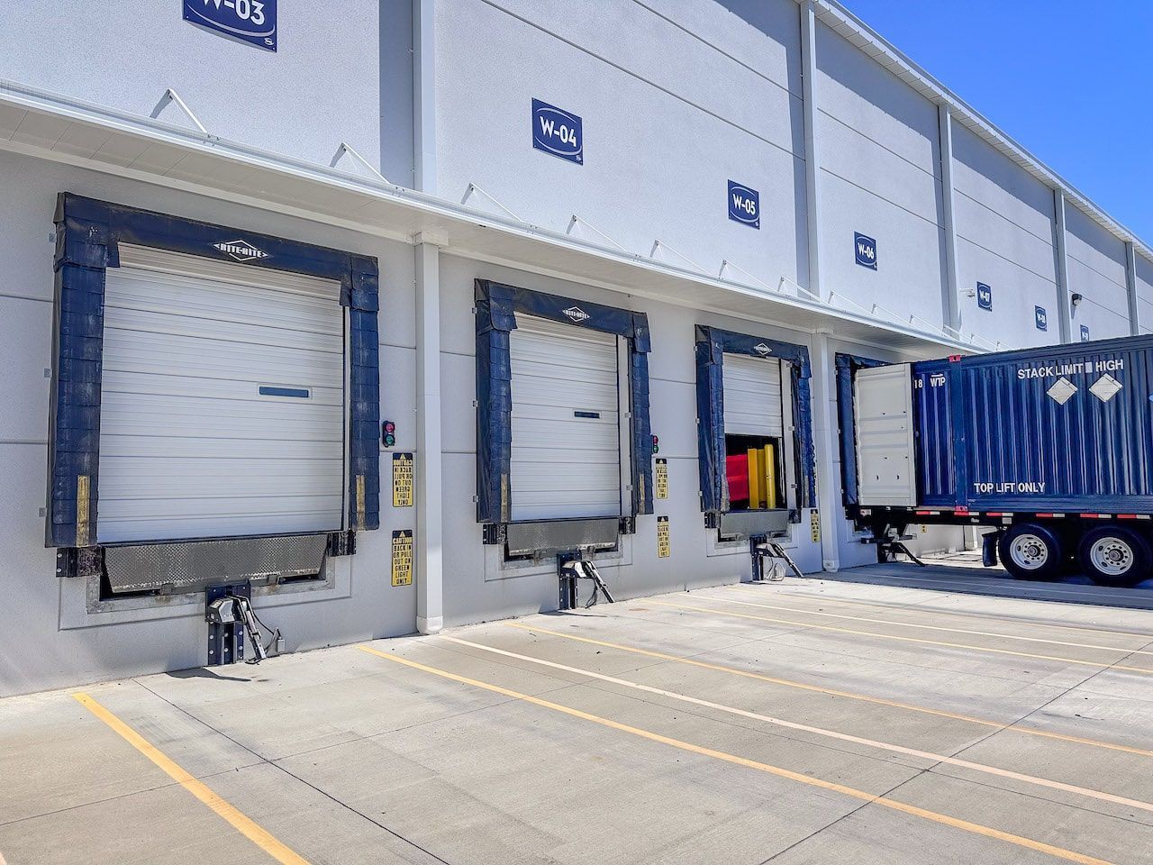 A truck is parked in front of a warehouse with docking doors open.