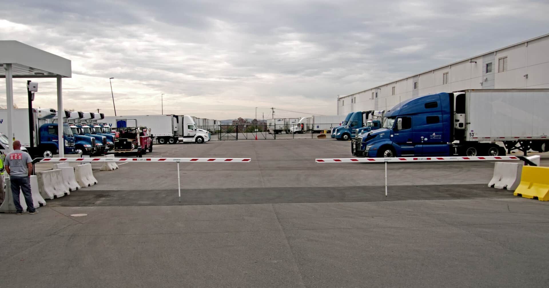 A lot of trucks are parked in a parking lot behind a barrier.