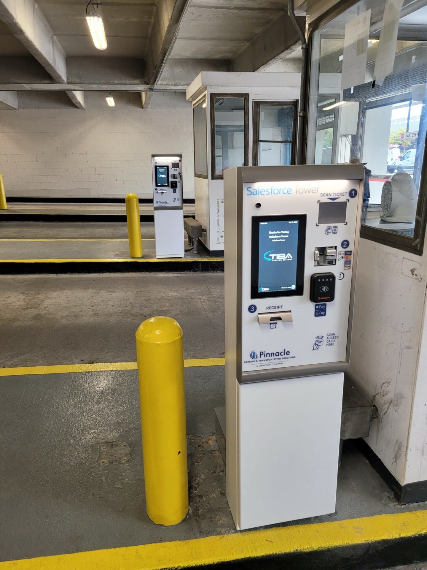 A parking meter is sitting in a parking garage next to a yellow pole.
