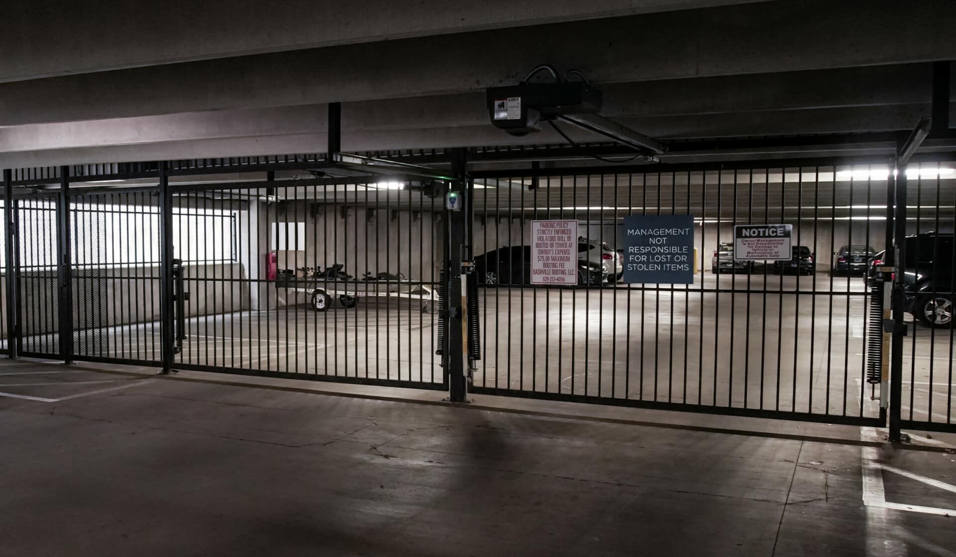 An empty parking garage with a fence and cars parked in it.