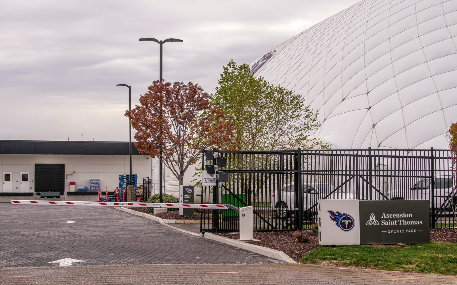 A large white building is behind a fence and a parking lot.