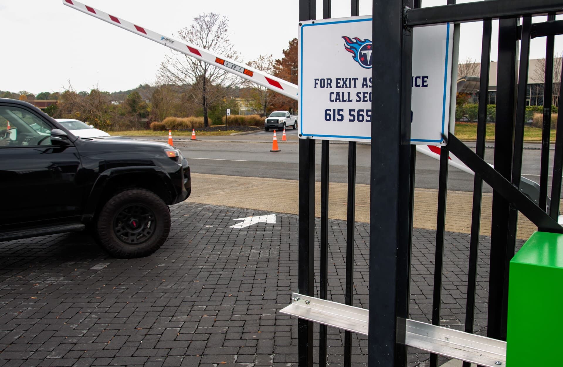 A black suv is driving through a gate with a sign that says for exit and call security 615 568