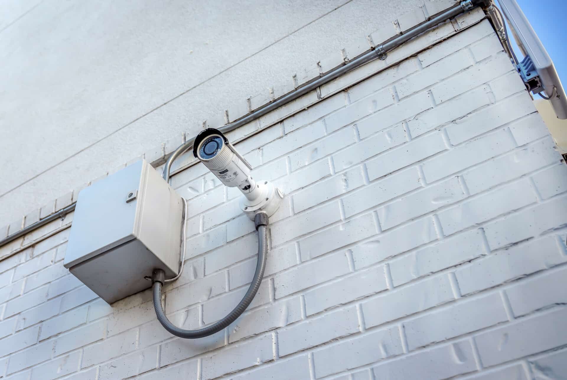 A security camera is mounted on the side of a white brick building.