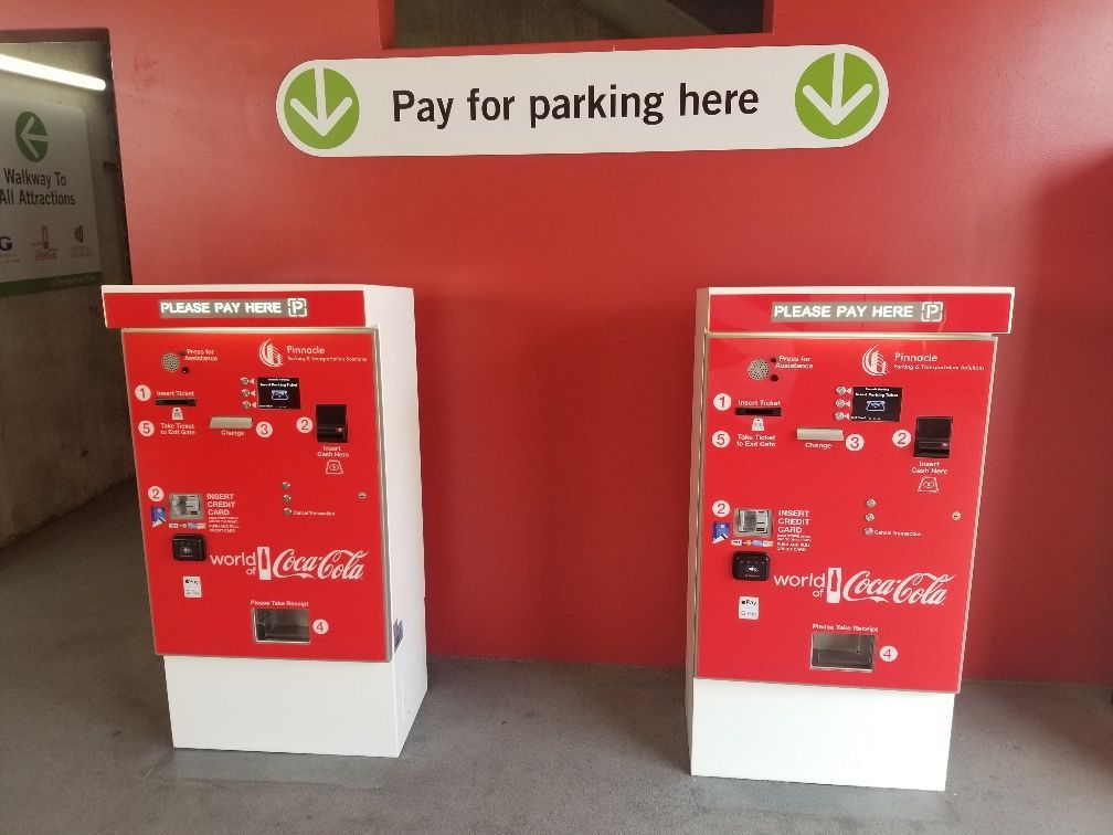 Two coca cola pay for parking machines in front of a sign that says pay for parking here