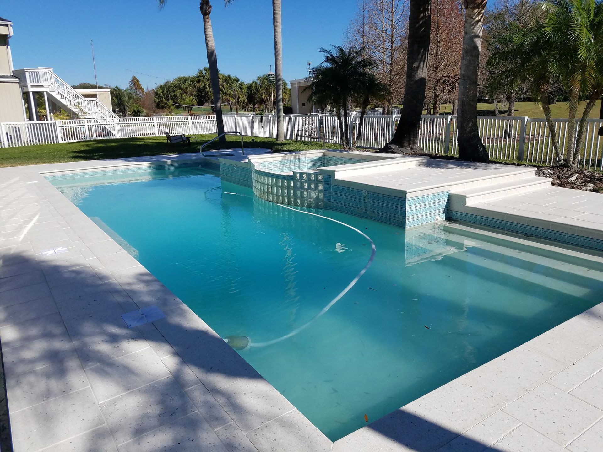 Blue swimming pool with built-in benches and a white deck in a sunny outdoor courtyard