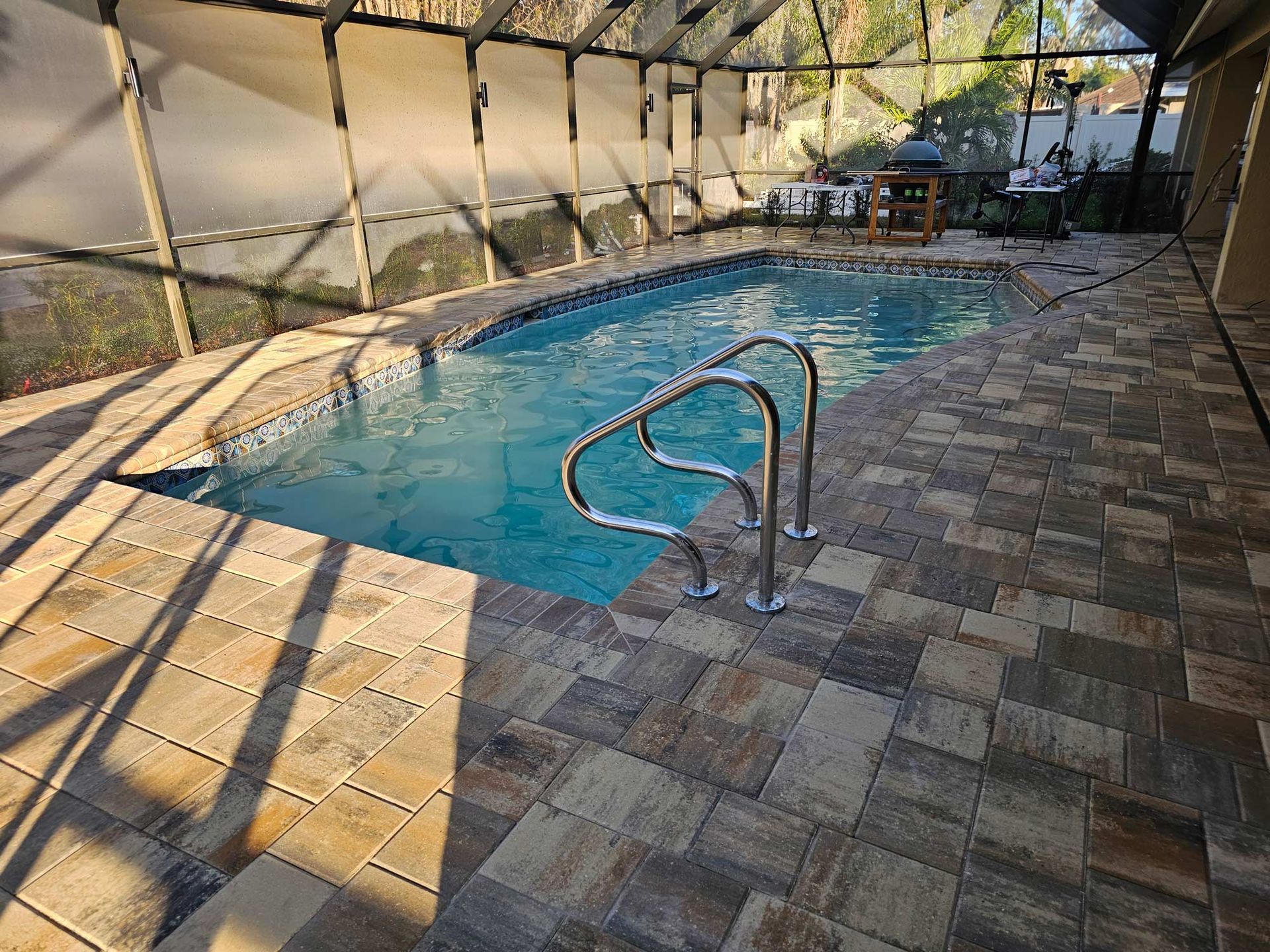 Outdoor swimming pool with blue water, stone deck, and metal handrails under a shaded enclosure