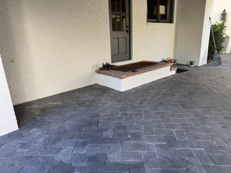 Covered patio with gray brick pavers, white walls, and a small front step leading to a door