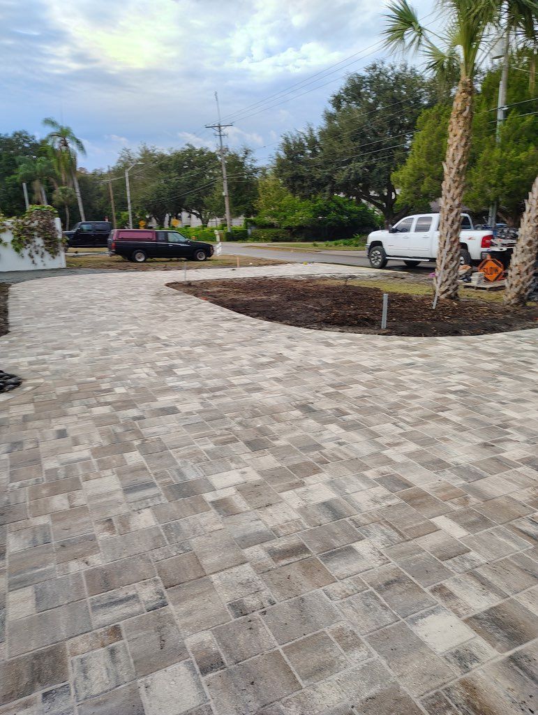 Stone-paved driveway or courtyard with parked vehicles and trees in a landscaped outdoor area.