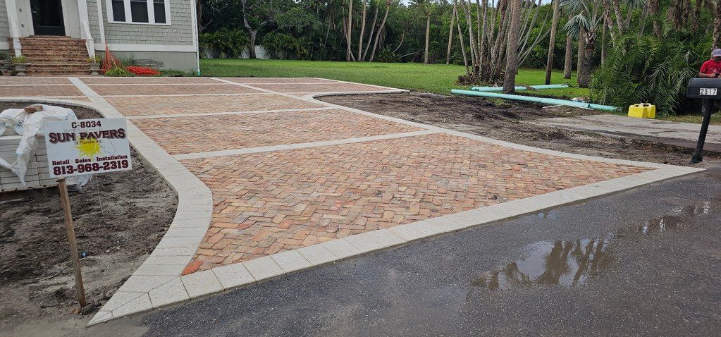 Freshly paved driveway and walkway beside a house, bordered by a curved concrete edge and wet street.