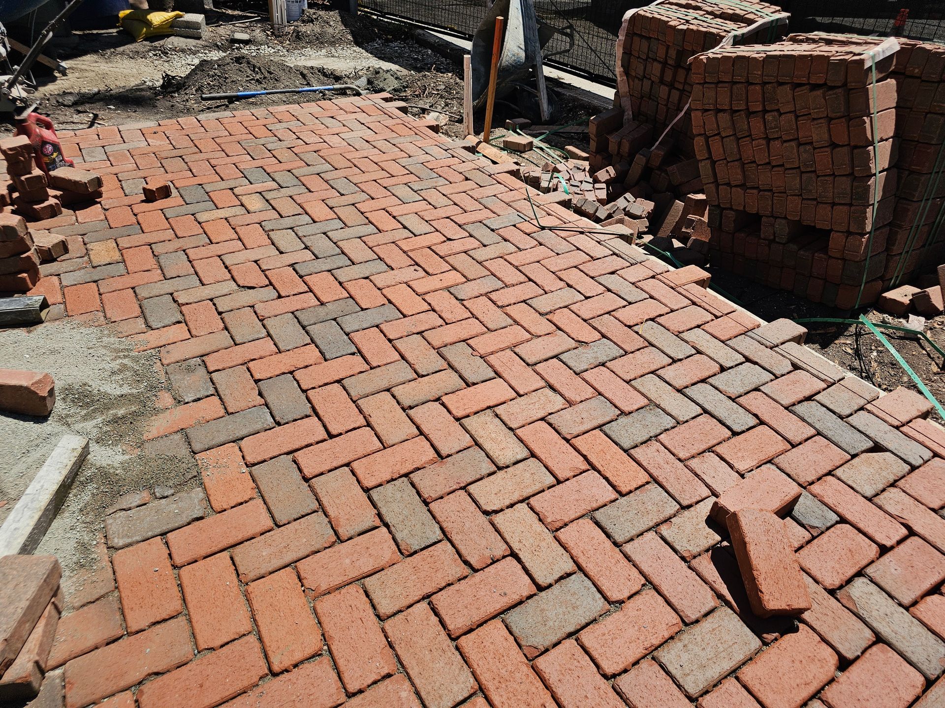 Brick walkway under construction with stacked red pavers and uneven ground beside it