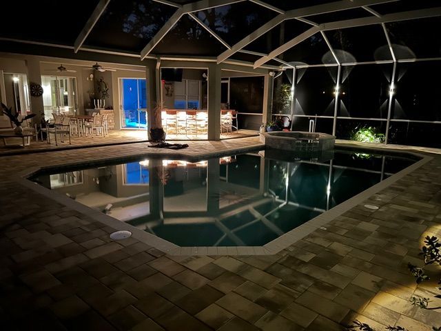 Indoor pool at night with warm lighting, tiled deck, and a screened enclosure