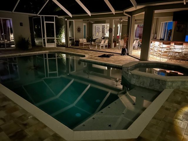 Nighttime backyard pool with hot tub and patio seating under a covered lanai.