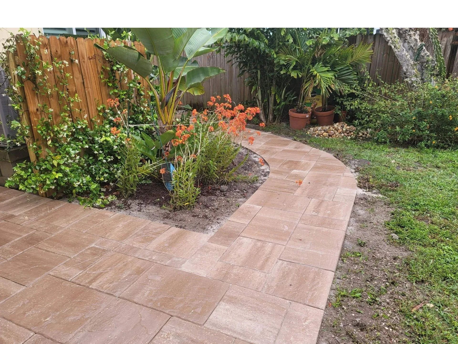 Curved stone garden path beside lush greenery, orange flowers, and a wooden fence