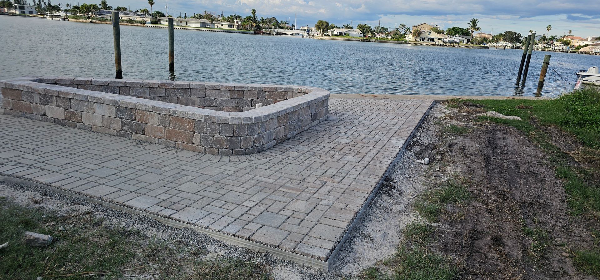 Stone platform beside a lake with paved walkway, grass, and distant houses across the water