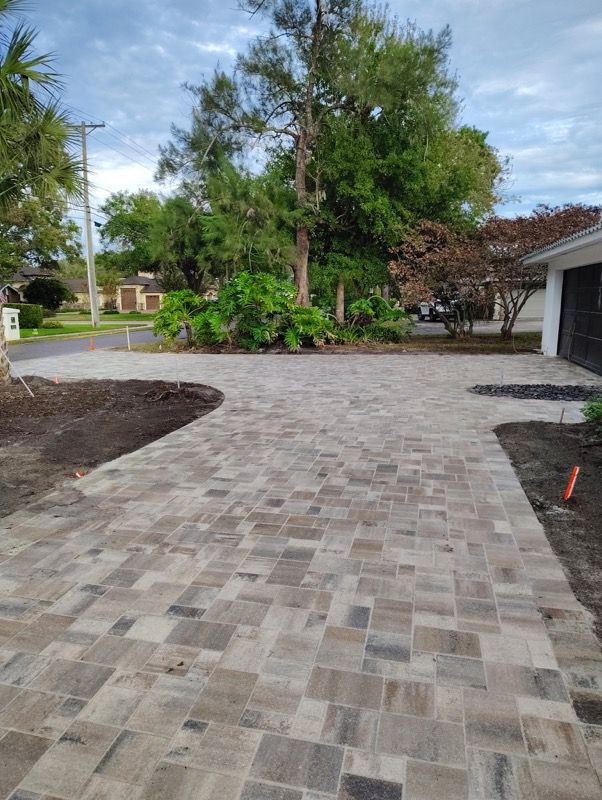 Paved driveway leading to a house, bordered by trees and landscaped greenery.