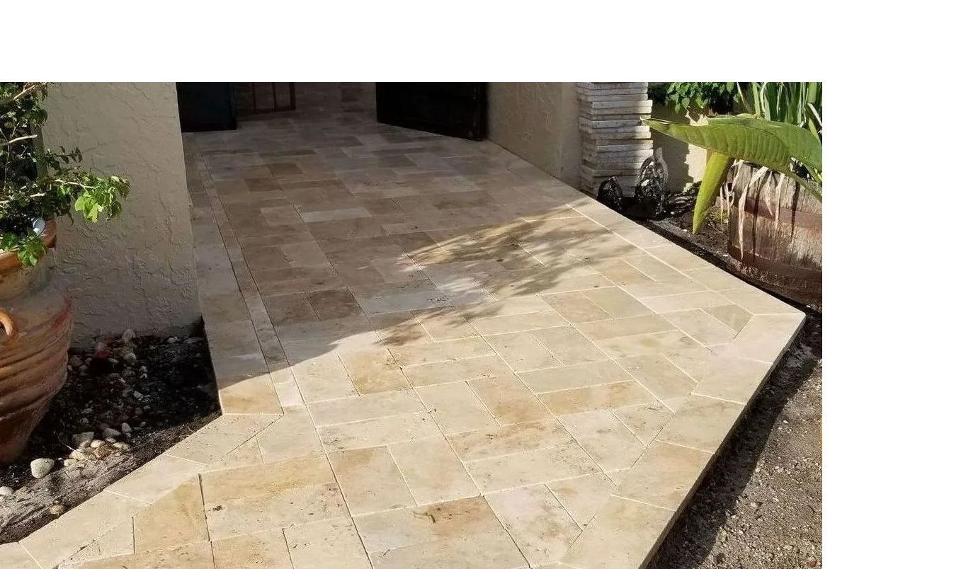 Stone-tiled front patio leading to a shaded entrance, with potted plants along the edges.