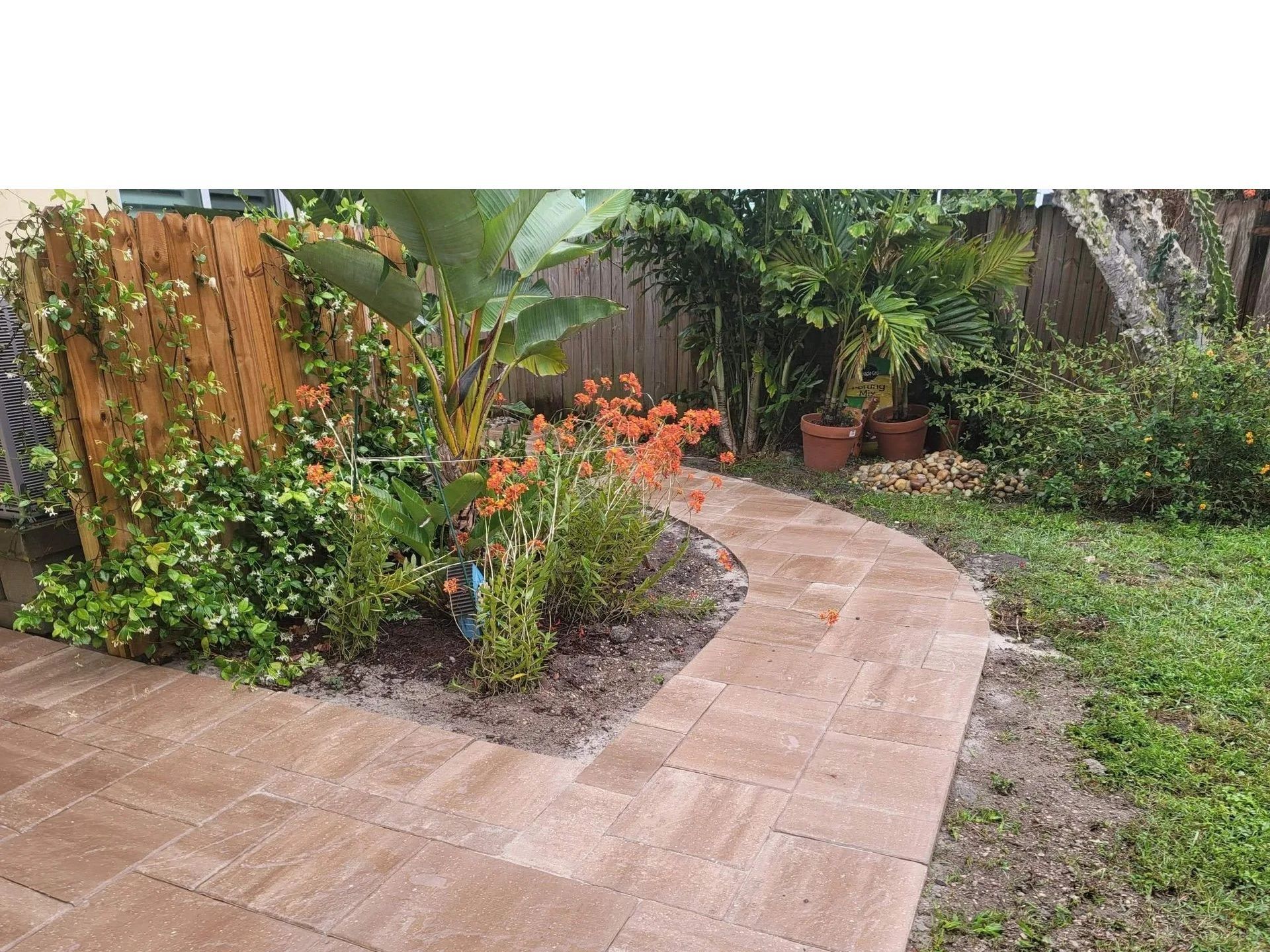 Curved brick garden path beside flower beds and potted plants in a backyard